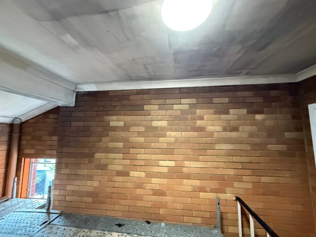 Smoke and soot staining on face brick and eaves in an Adamstown apartment stairwell before dry ice blasting