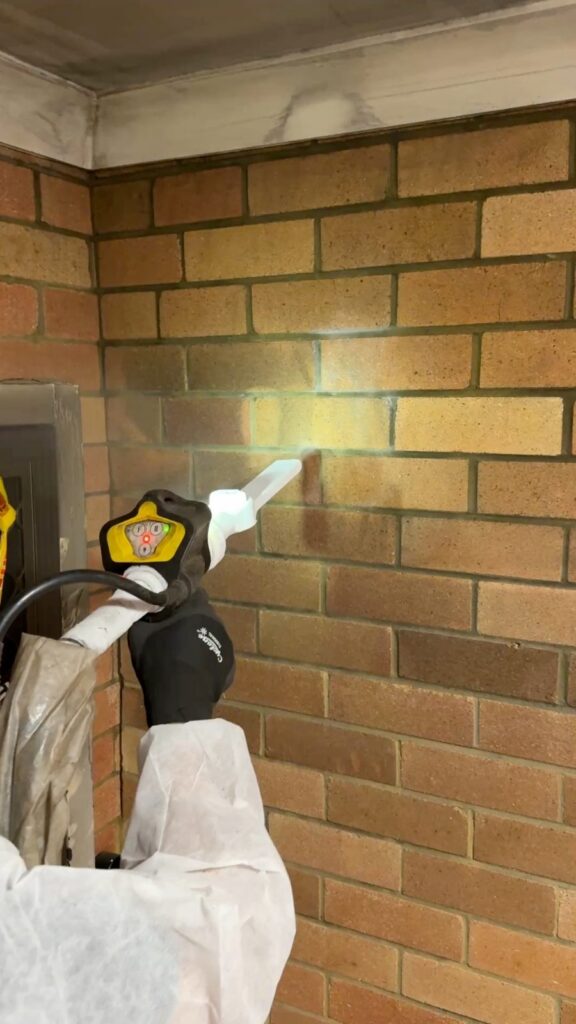 CDCR technician in full PPE dry ice blasting soot from face brick