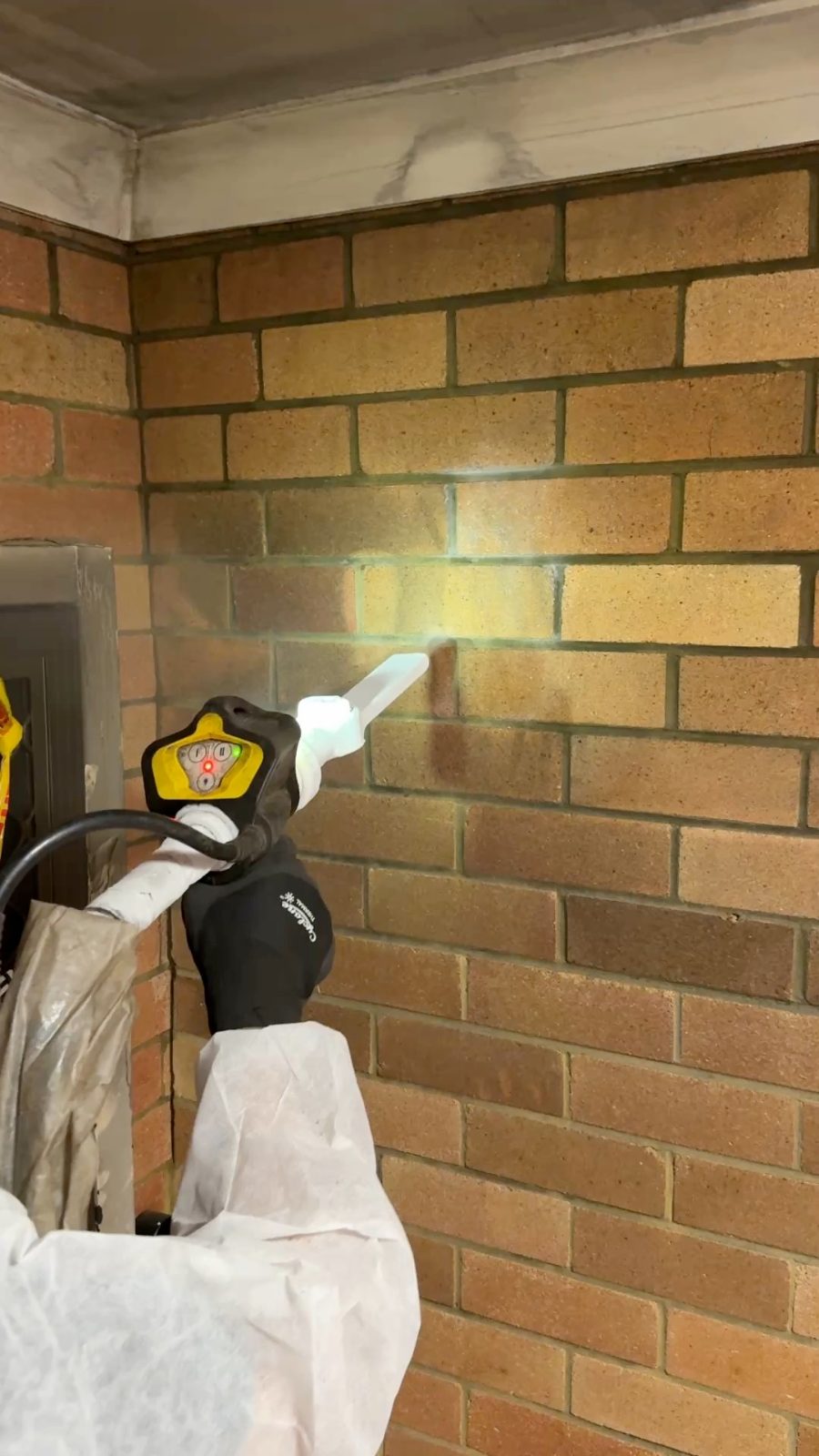 CDCR technician in full PPE dry ice blasting soot from face brick